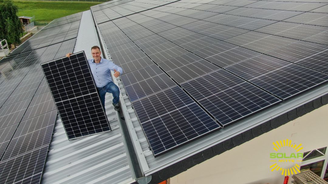 Ein Gebäude, das mit Solarmodulen ausgestattet ist. Auf dem Dach steht ein Mann, der ein Solarmodul in den Händen hält.