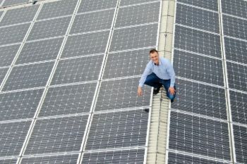 Ein Mann sitzt auf einem Dach mit Solarmodulen und schaut in die Kamera